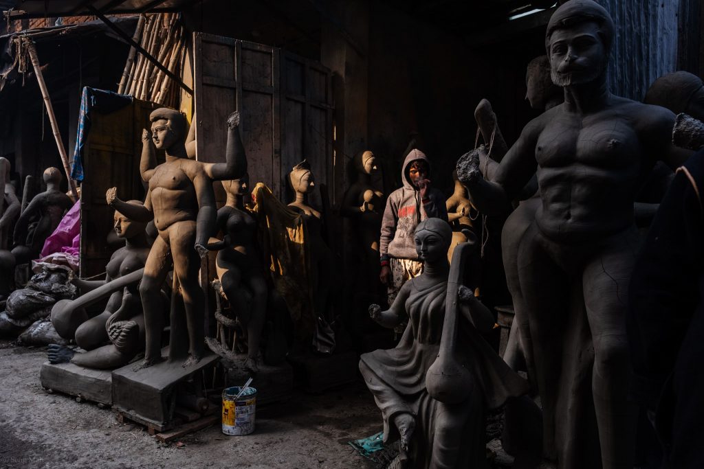 A man stands in the shadows of a clay effigy shop in Kumartolli, Kolkata