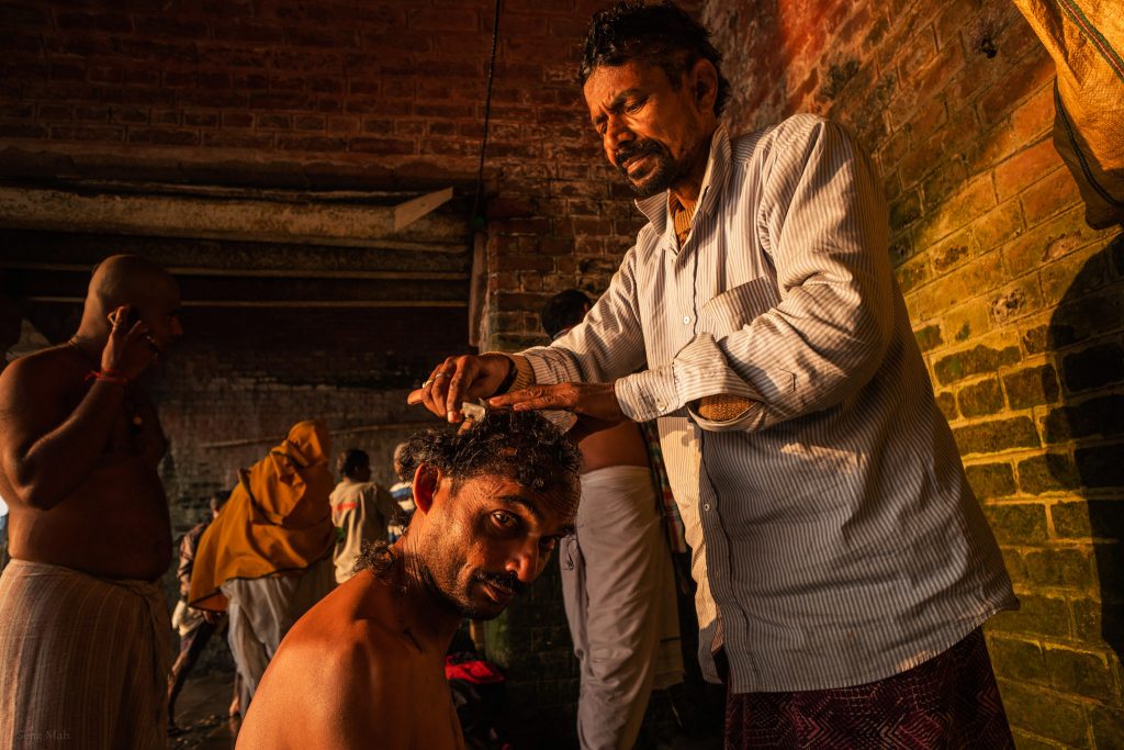 A barber shaves a man's head under the Hooghly Bridge in Kolkata.
