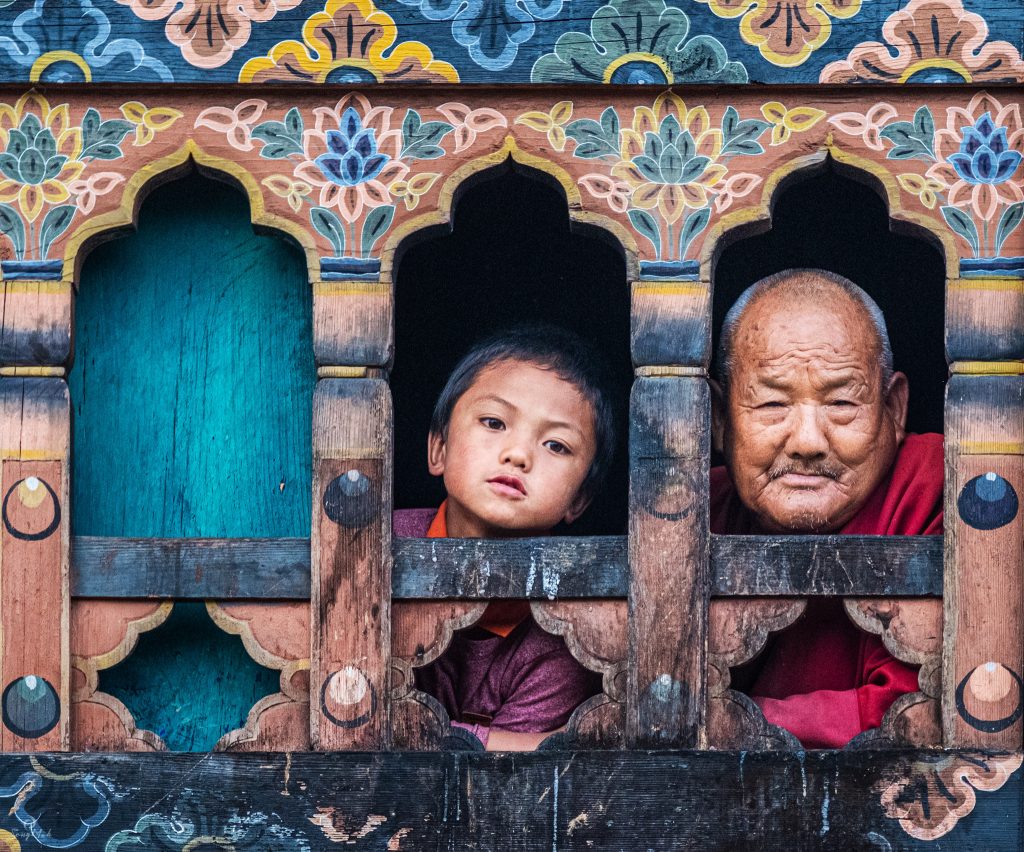 Boy and grandfather looking out of traditional Bhutanese windows.