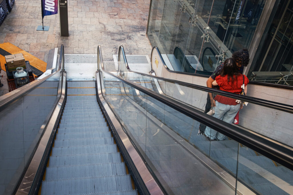 Street photograph of a couple embracing while riding up an escalator.
